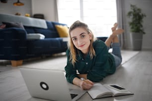 A young woman student with laptop and smartphone at home, home office and learning, looking at camera,