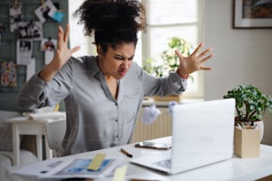 Frustrated young woman with laptop working indoors at home, home office concept.