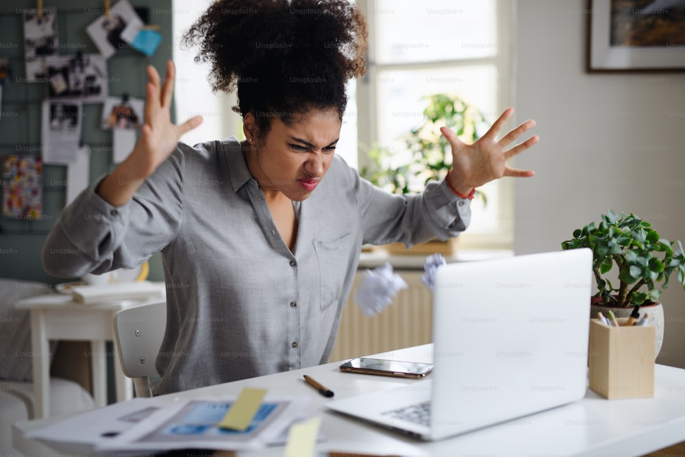 Jeune femme frustrée avec un ordinateur portable travaillant à l’intérieur à la maison, concept de bureau à domicile.