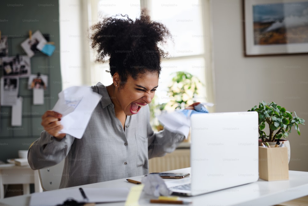 Frustrated young woman with laptop working indoors at home, home office concept.