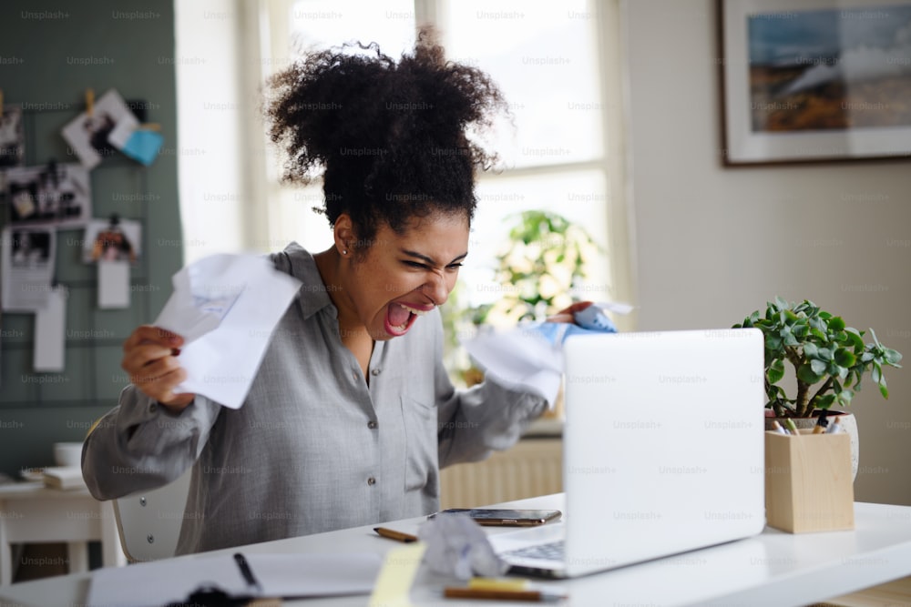 Frustrierte junge Frau mit Laptop, die drinnen zu Hause arbeitet, Home-Office-Konzept.