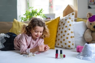 Menina pequena feliz dentro de casa, brincando na cama com acessórios. Conceito de lockdown.