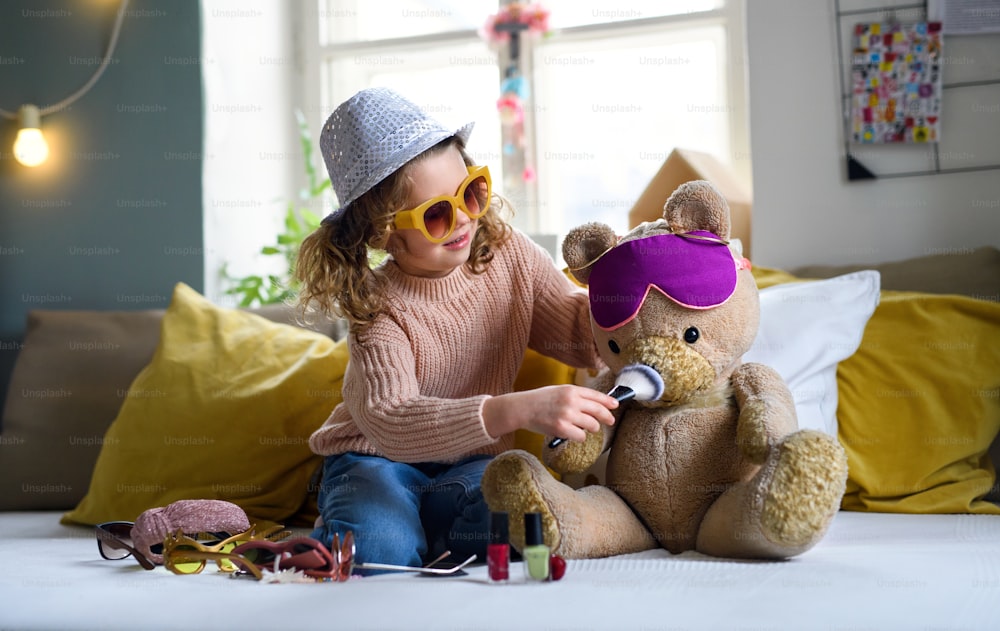 Portrait of small girl indoors at home, playing with teddy bear. Lockdown concept.