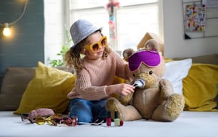 Portrait of small girl indoors at home, playing with teddy bear. Lockdown concept.