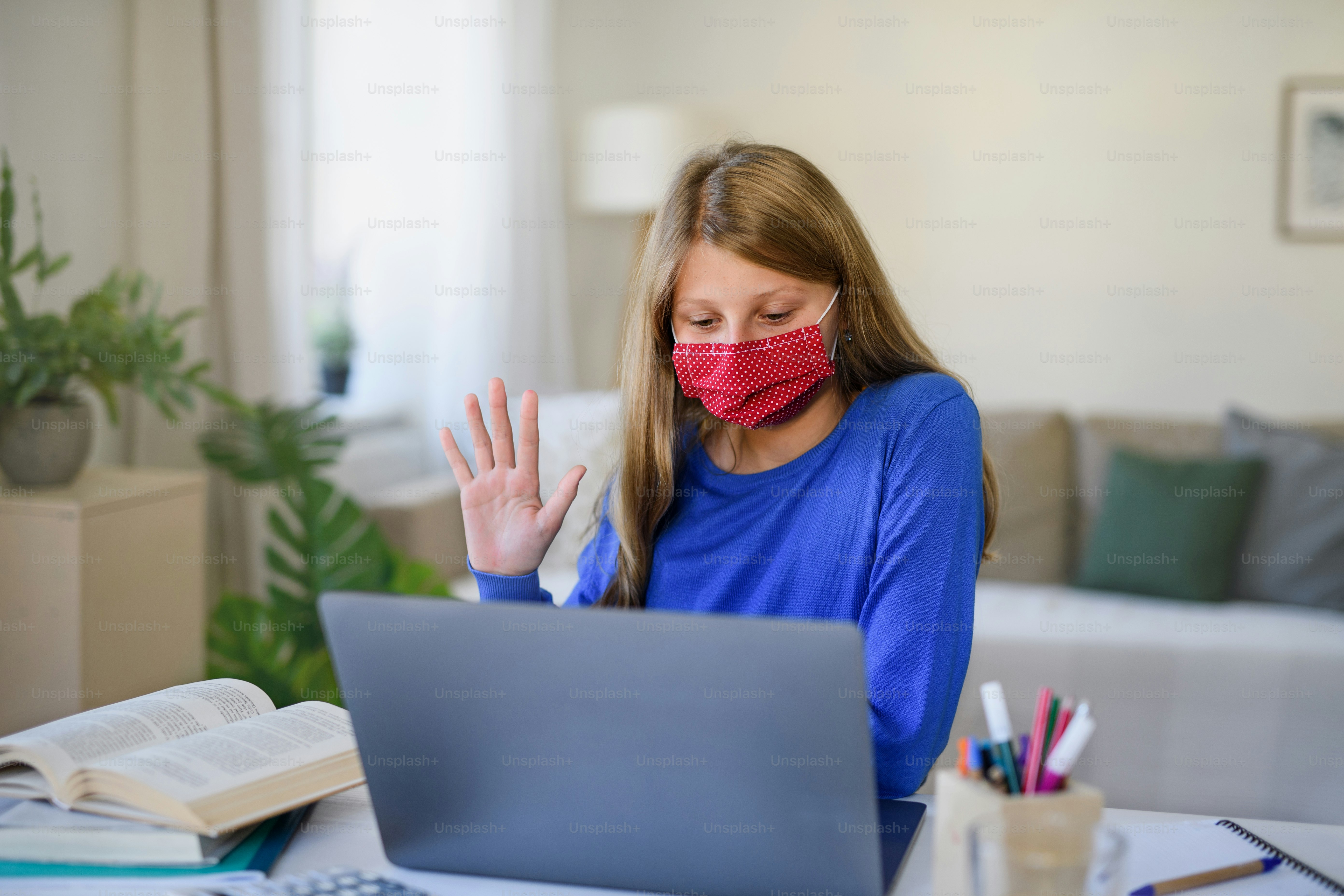 Schoolgirl with face mask learning online indoors at home, coronavirus concept.