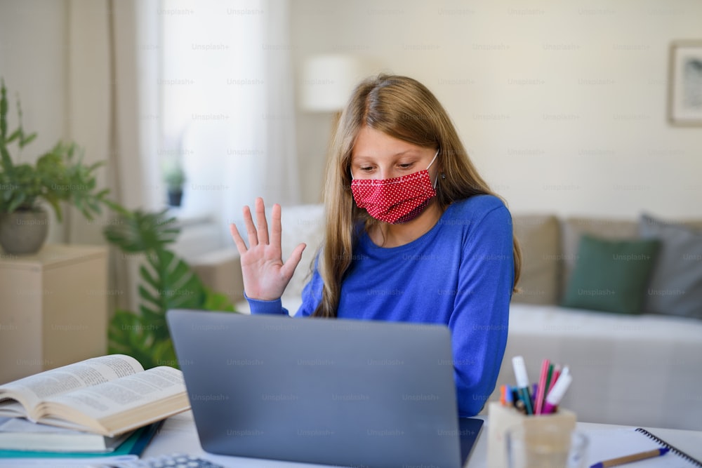 Studentessa con maschera facciale che impara online al chiuso a casa, concetto di coronavirus.