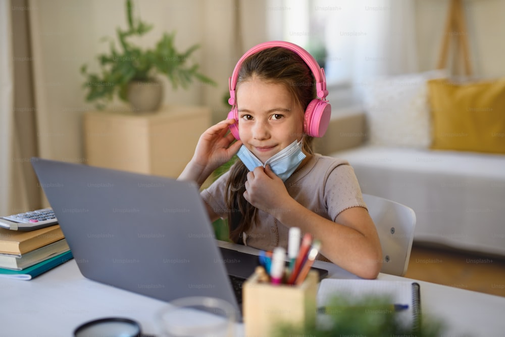 Schoolgirl having online lesson indoors at home, greeting teacher and coronavirus concept.