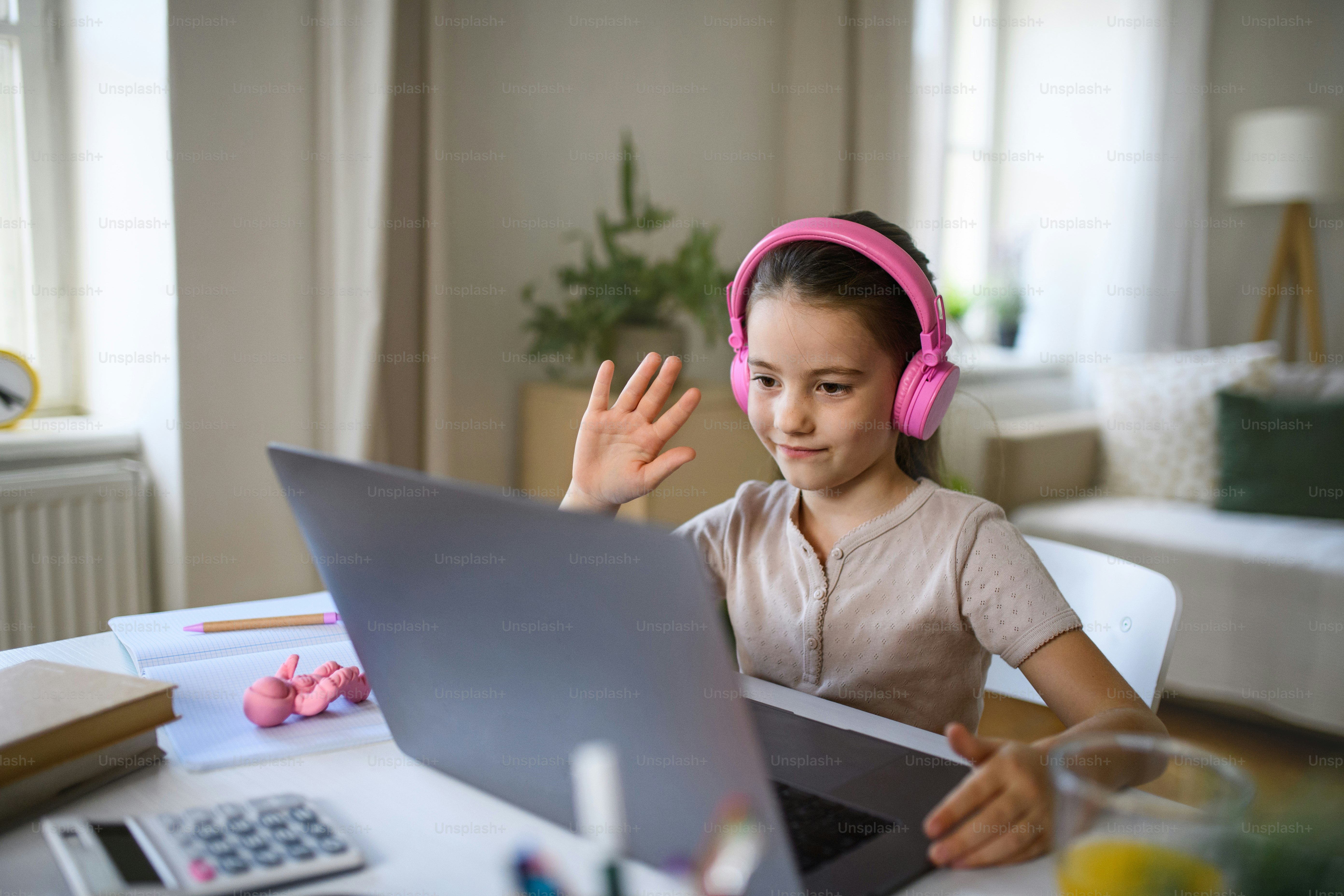 Schoolgirl having online lesson indoors at home, greeting teacher and coronavirus concept