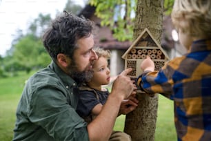 Happy small children with father holding bug and insect hotel in garden, sustainable lifestyle.