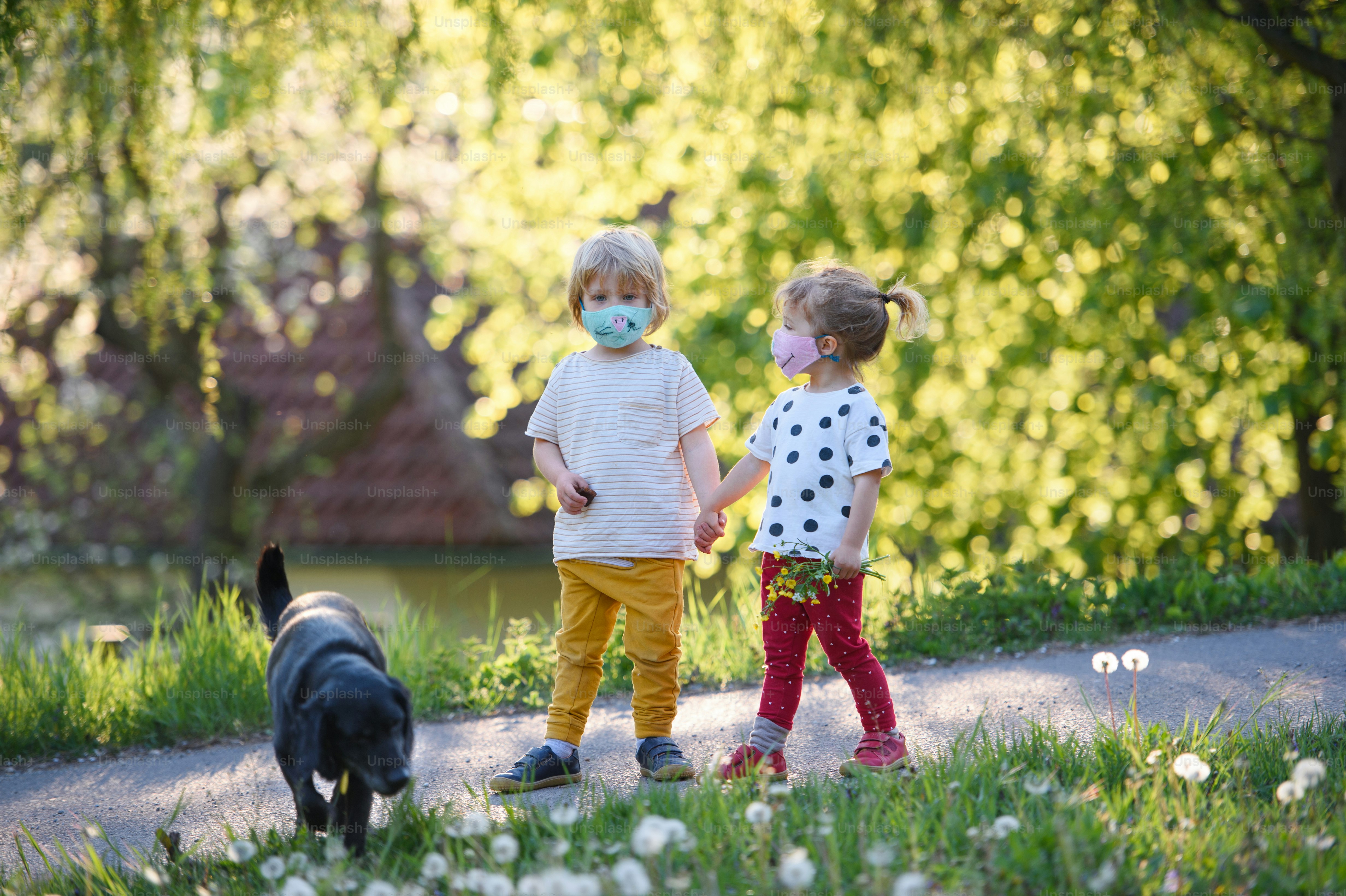 Small children with face masks and dog playing outdoors in countryside ...