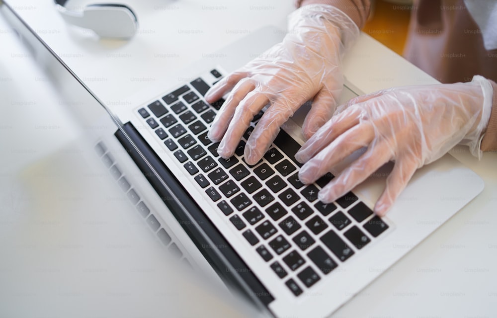 Hands of unrecognizable woman with gloves at the table, using laptop in quarantine.