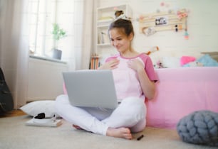 Front view of young girl with laptop sitting on floor, relaxing during quarantine.