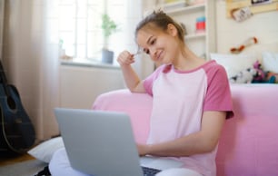 Front view of young girl with laptop sitting on floor, relaxing during quarantine.