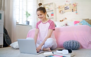 Vista frontal da menina com laptop sentado no chão, relaxando durante a quarentena.