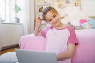 Vue de face d’une jeune fille avec un ordinateur portable assise par terre, se relaxant pendant la quarantaine.
