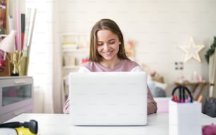 Front view of young female student sitting at the table, using laptop in quarantine.