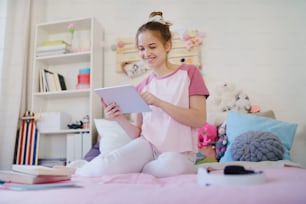 Young girl with tablet sitting and relaxing on bed, quarantine concept.