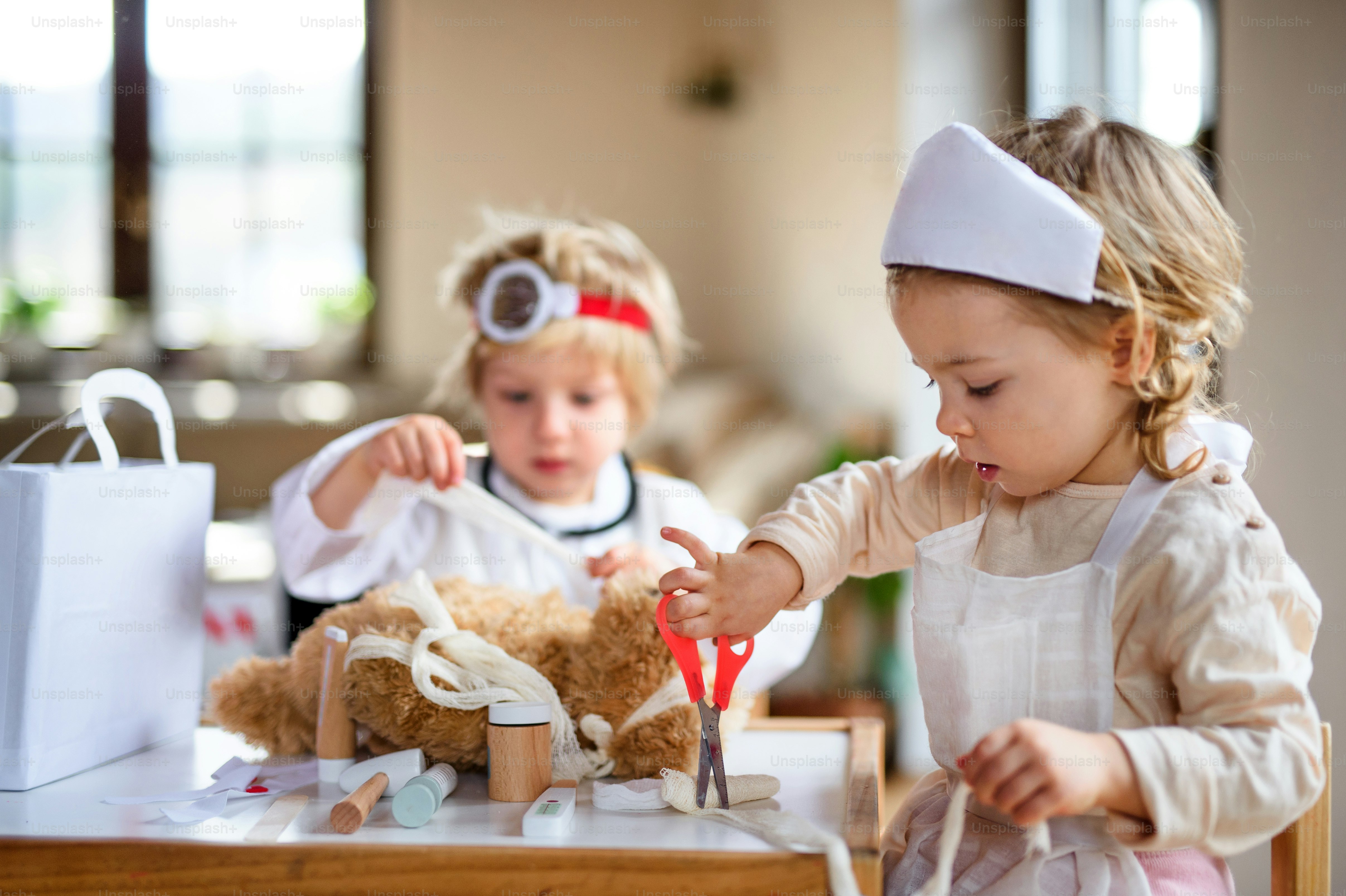 Deux jeunes enfants avec des uniformes de médecin et un stéthoscope à l’intérieur à la maison, en train de jouer.