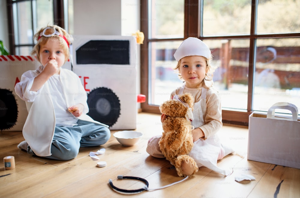 Two small children with doctor uniforms and stethoscope indoors at home, playing.