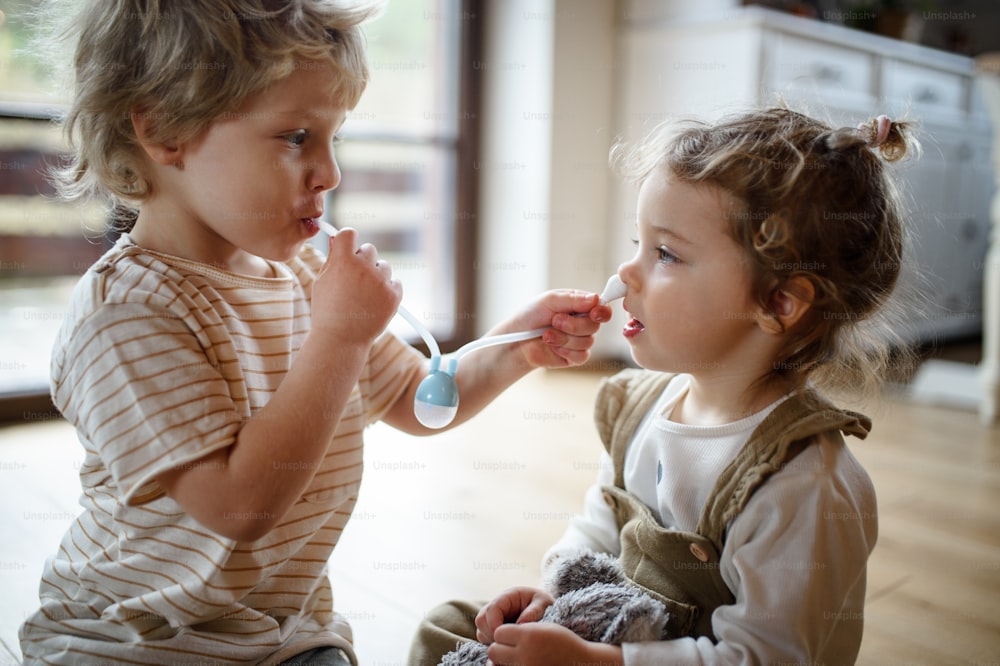 Deux jeunes enfants frère et sœur à l’intérieur à la maison, jouant avec un aspirateur nasal.