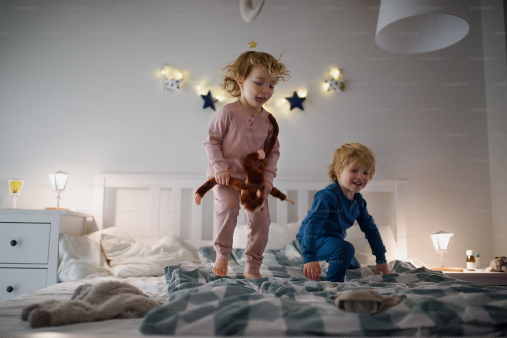 Dos pequeños niños riendo saltando en la cama en el interior de casa, divirtiéndose.