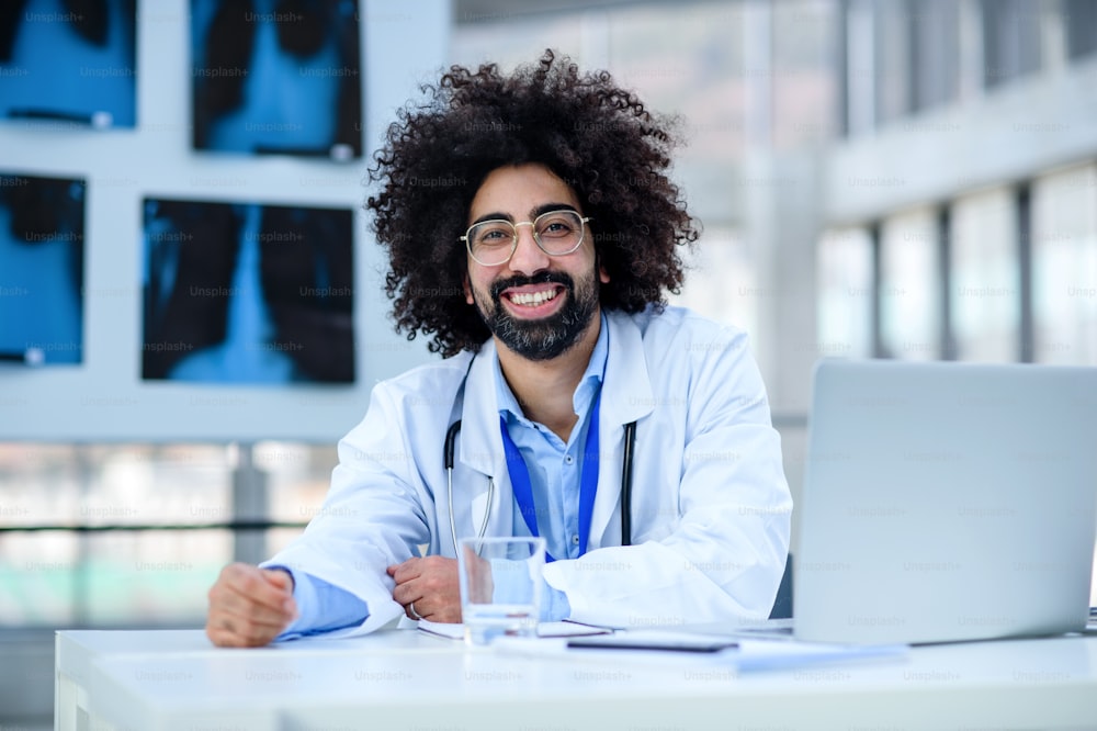 Vorderansicht Porträt eines fröhlichen männlichen Arztes, der im Krankenhaus sitzt und in die Kamera schaut.