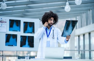 Portrait of male doctor looking at X-ray in hospital, corona virus concept.