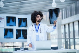 Portrait of male doctor looking at X-ray in hospital, corona virus concept.