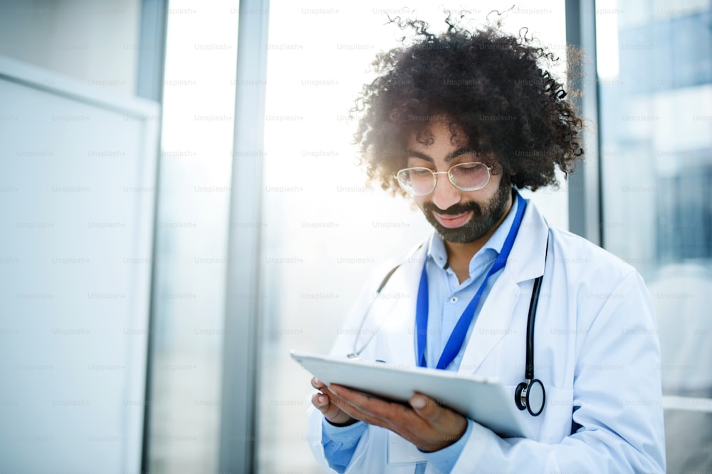 Ritratto di medico maschio in piedi in ospedale, usando tablet. Copia spazio.
