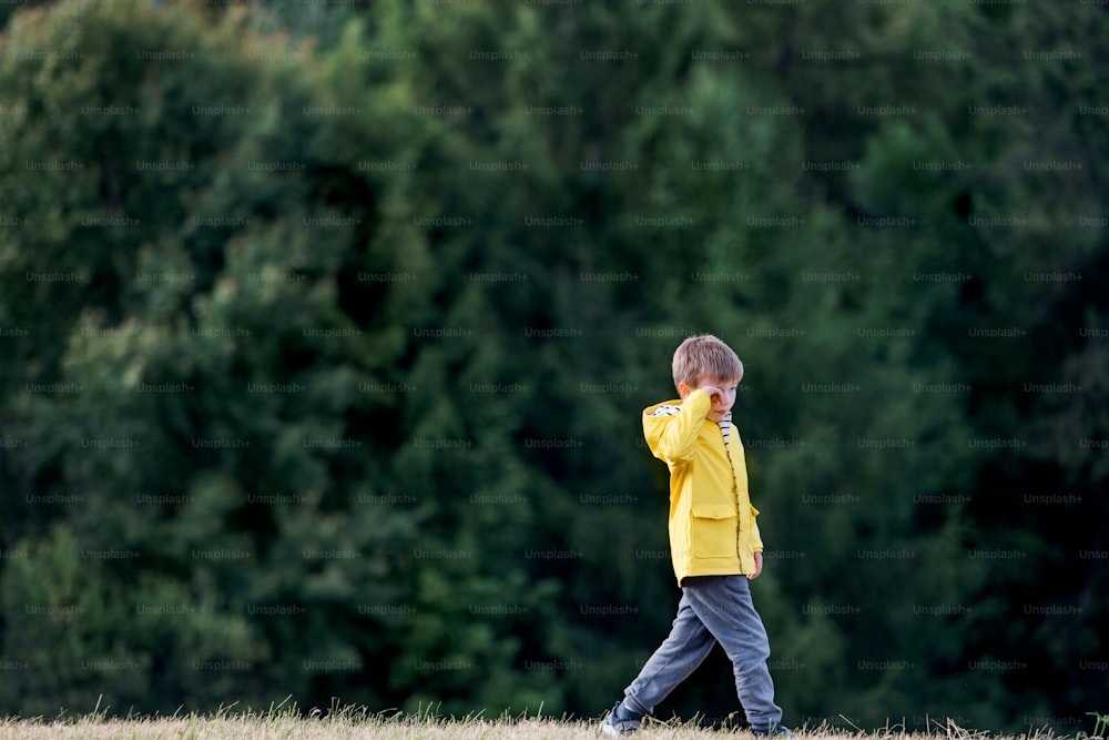Side view of sad school child walking on field trip in nature, rubbing eyes.