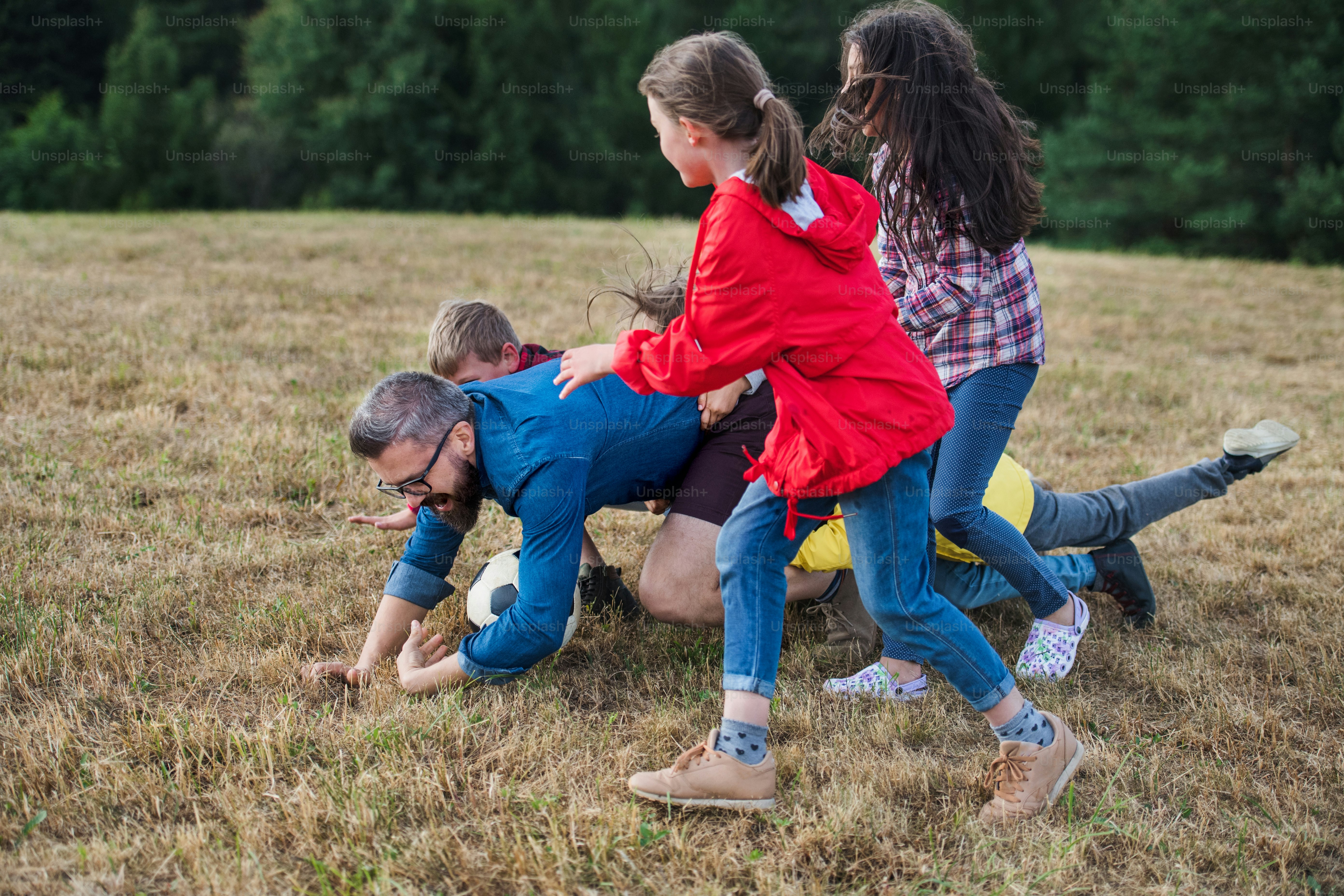 Um grupo de crianças pequenas em idade escolar com professor em viagem de campo na natureza, brincando com uma bola.