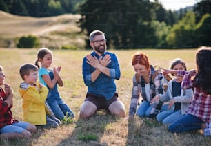 A group of small school children with teacher on field trip in nature, chanting.