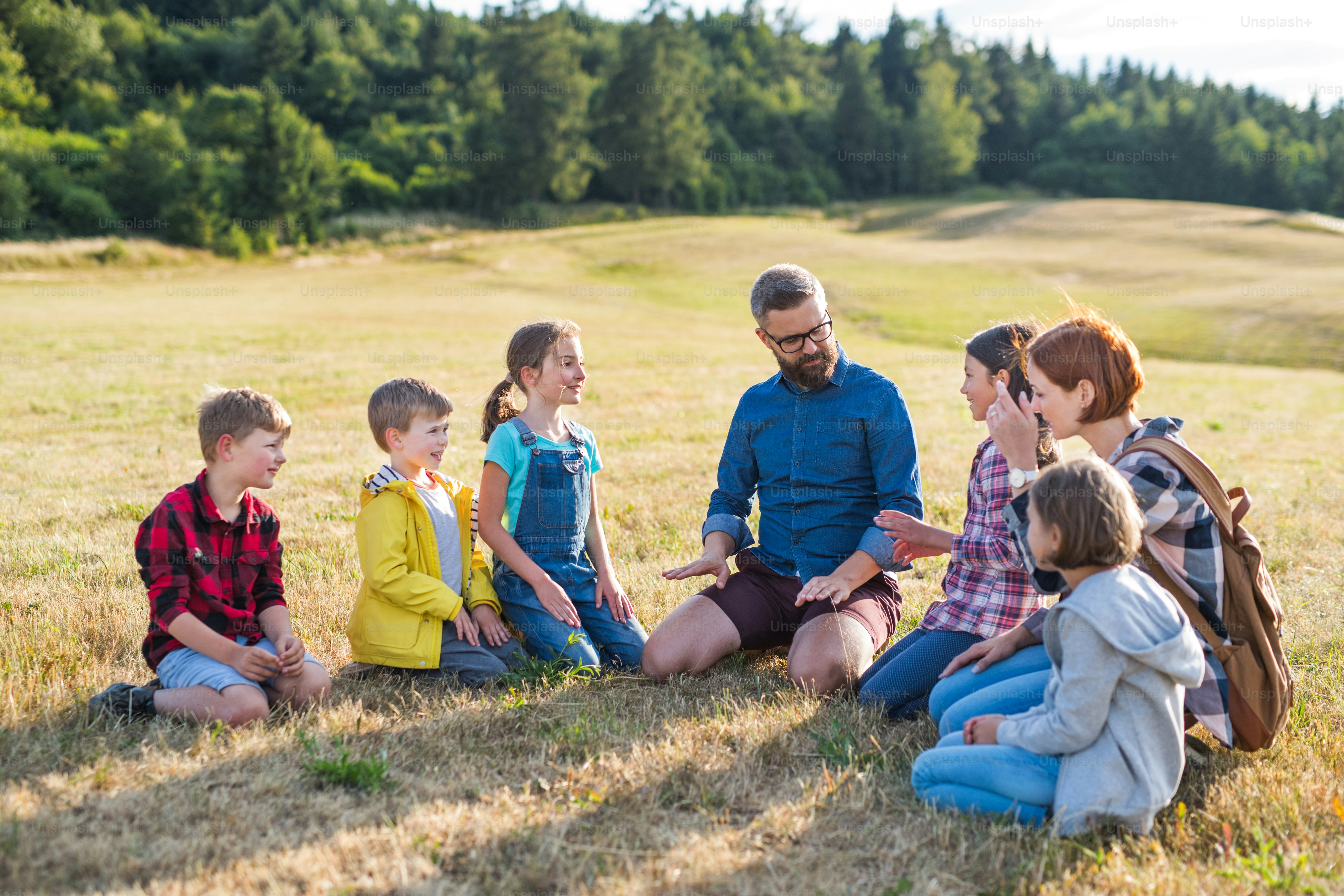 Grupo de crianças em idade escolar com professor em viagem de campo na natureza, sentado e conversando.