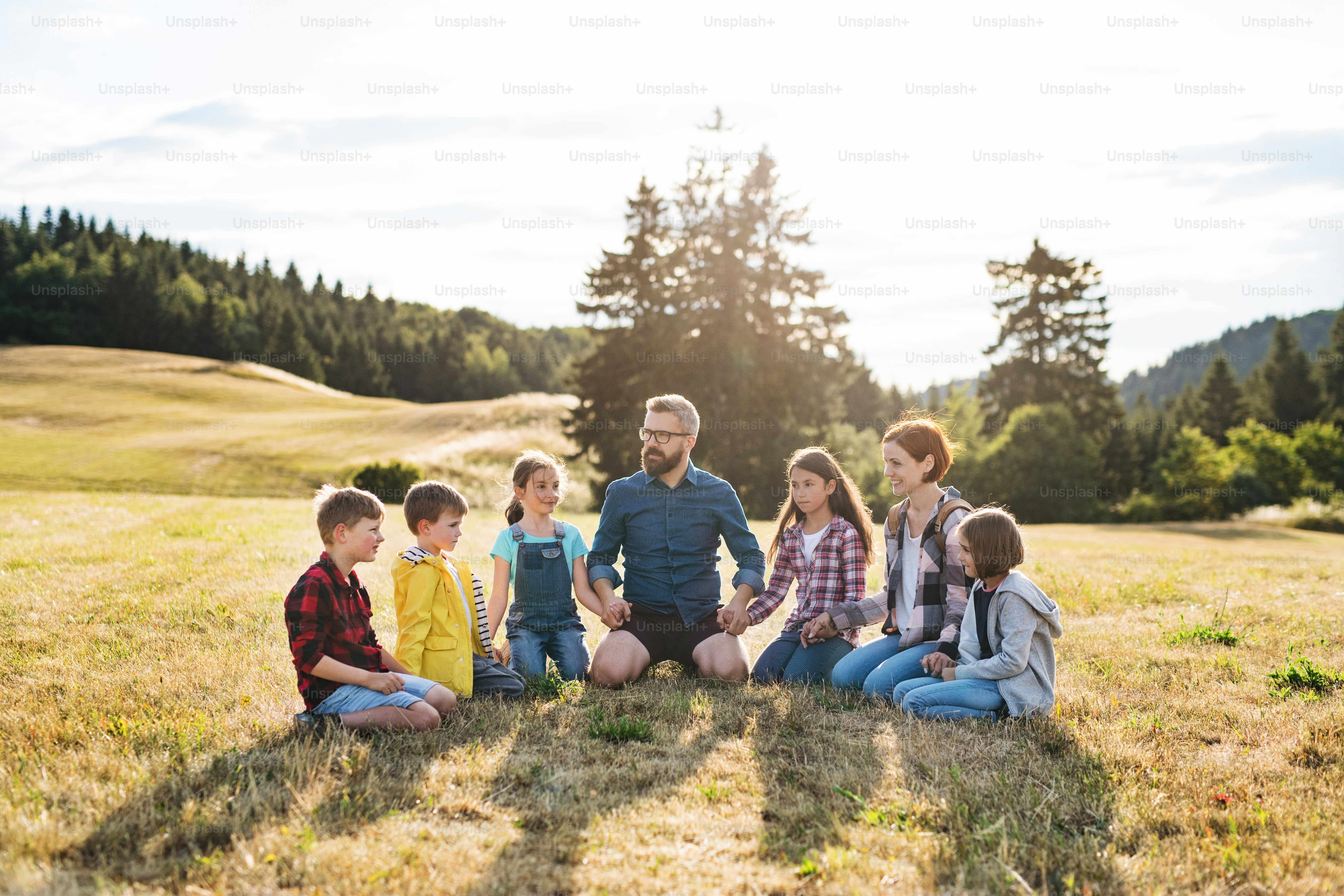Grupo de crianças em idade escolar com professor em viagem de campo na natureza, sentado e de mãos dadas.