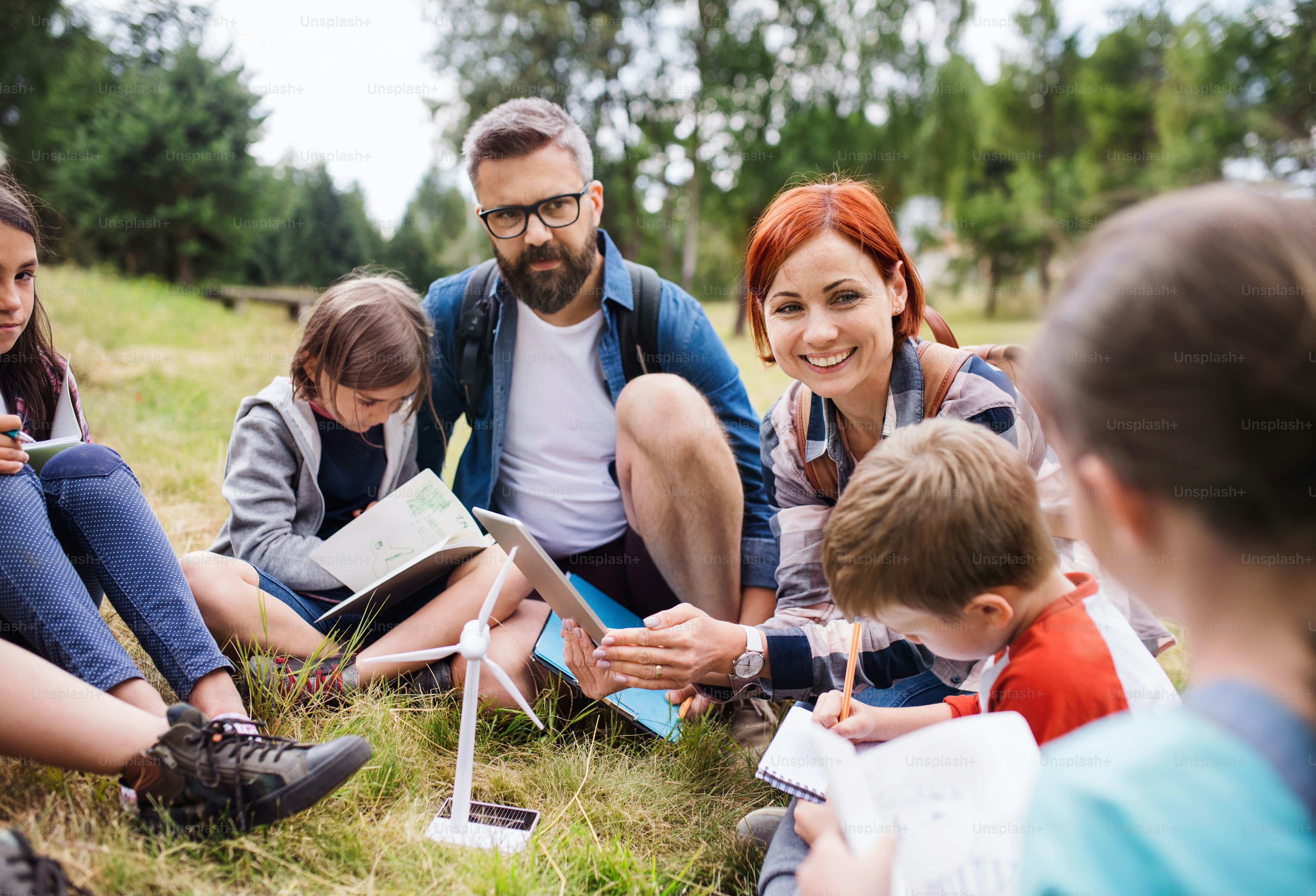 Um grupo de crianças em idade escolar com modelo de professor e moinho de vento em viagem de campo na natureza.