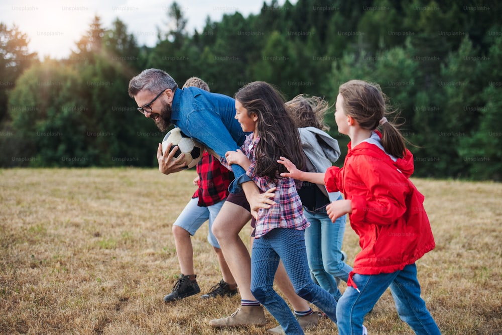 A group of small school children with teacher on field trip in nature, running.