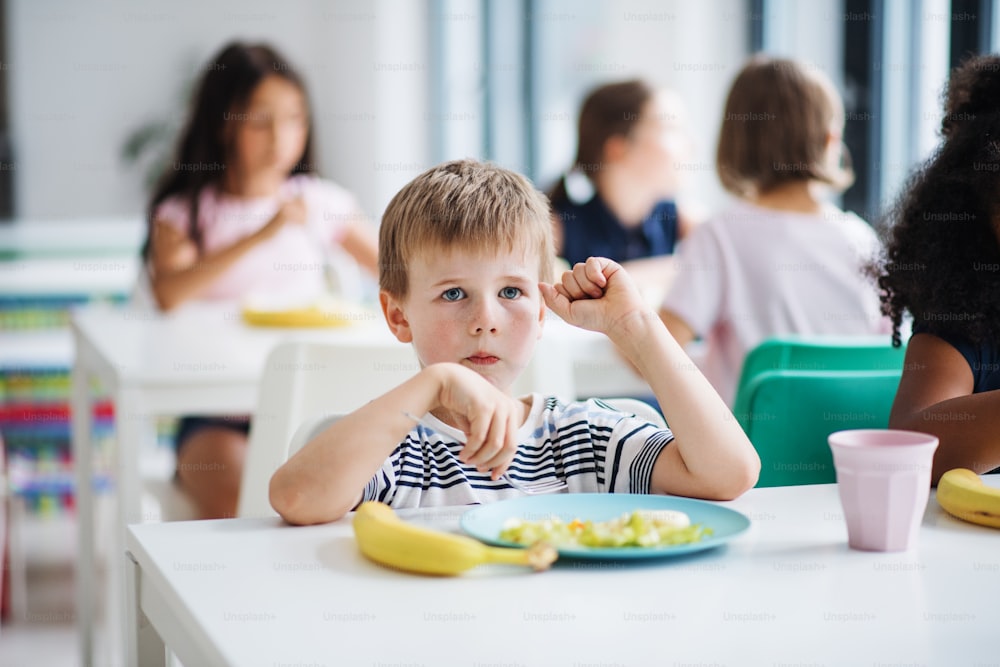 Um grupo de alegres crianças de pequenas escolas na cantina, almoçando e conversando.