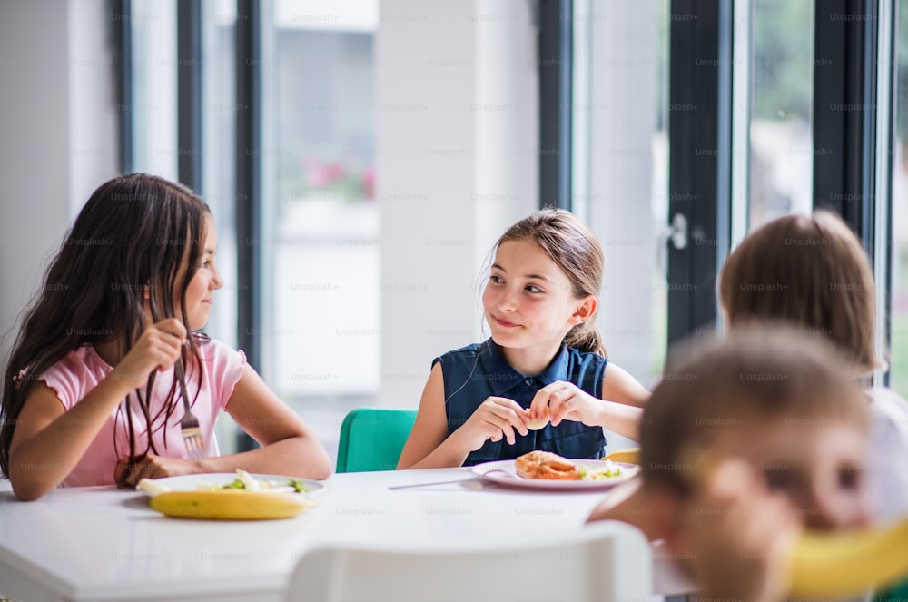 Un grupo de niños alegres de la escuela pequeña en la cantina, almorzando y hablando.