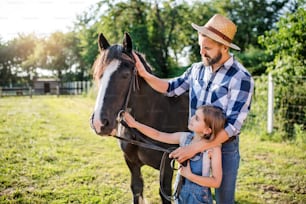 A mature father and small daughter with horse working on small family animal farm.