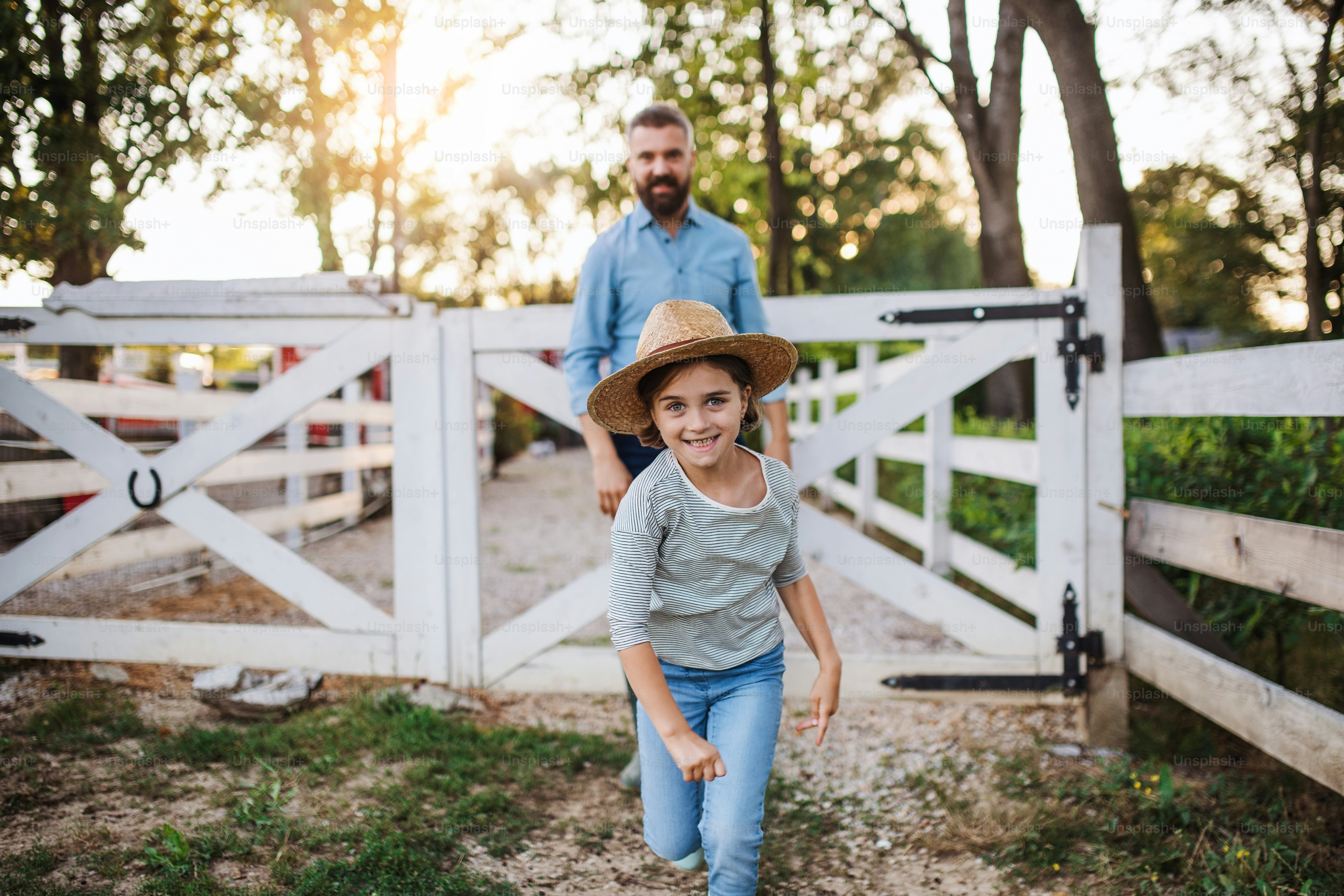 Una vista frontale del padre maturo e della piccola figlia con gli stivali di gomma che camminano all'aperto nella piccola fattoria di famiglia.