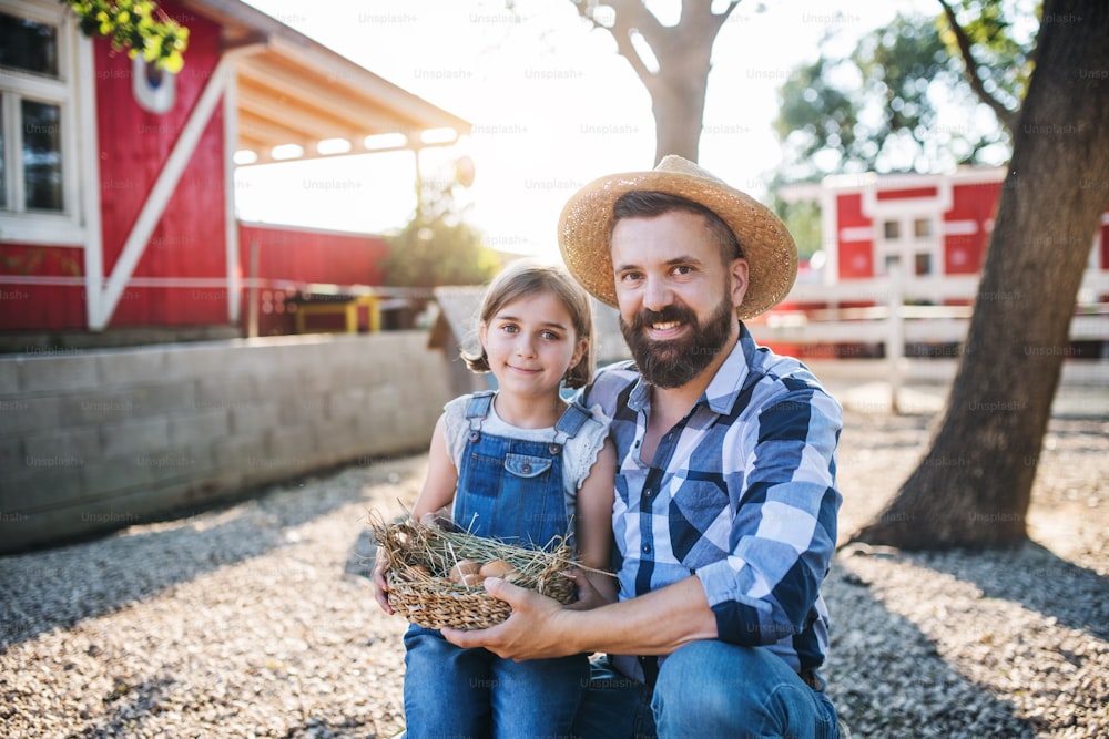 A father with small daughter outdoors on family farm, holding basket with eggs.