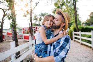 A mature father with small daughter walking outdoors on family farm.