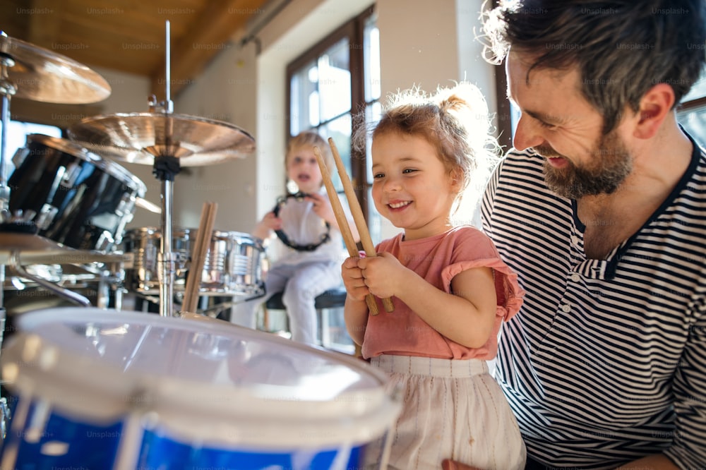 Retrato de niños pequeños felices con el padre en el interior de casa, tocando la batería.