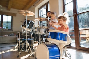 Porträt eines glücklichen kleinen Mädchens drinnen zu Hause, das Schlagzeug spielt.
