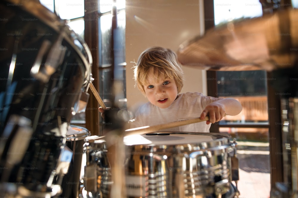 Vista frontal de un niño pequeño feliz en el interior de su casa, tocando la batería.