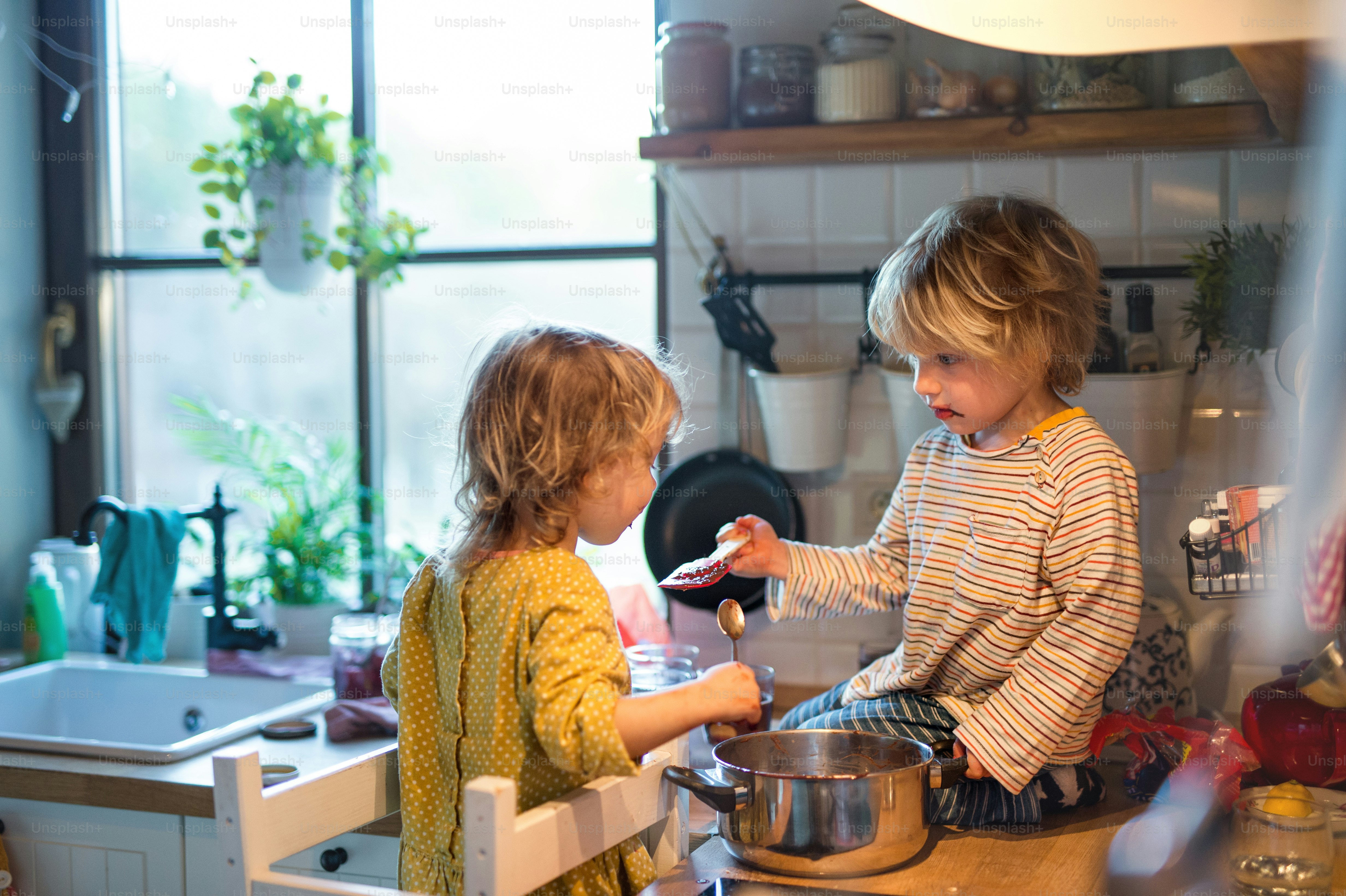 Happy small boy and girl indoors in kitchen at home, helping with cooking.