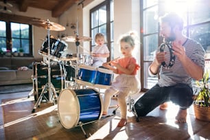 Portrait of happy small children with father indoors at home, playing drums.