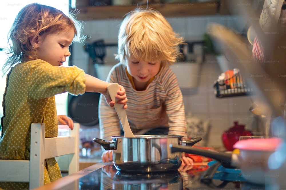 Menino e menina pequenos felizes dentro de casa na cozinha em casa, ajudando com a cozinha.
