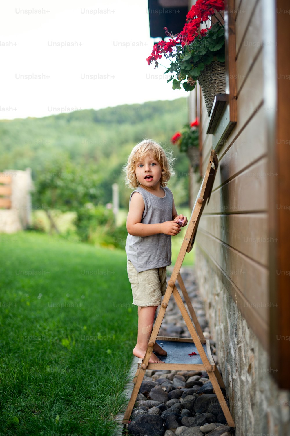 Portrait of happy small blond boy playing outdoors by house in summer.