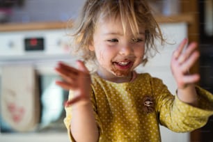 Petite fille joyeuse avec la bouche sale à l’intérieur dans la cuisine à la maison, applaudissant.